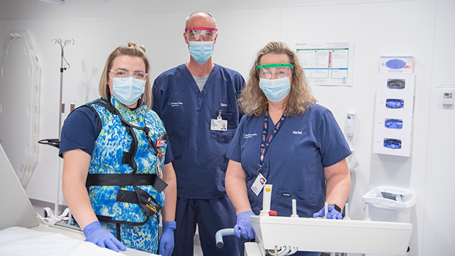 Team of medical professionals, two women and one man, in a medical exam room wearing blue scrubs